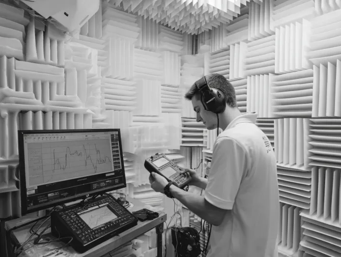 Technician conducting sound measurements in anechoic chamber with analysis equipment