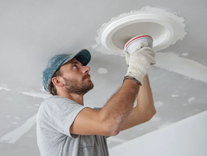 Worker sealing a light fixture cutout in a soundproofed drywall ceiling